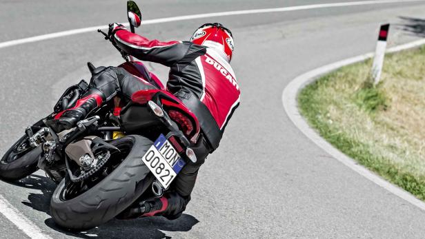 Ein Motorradfahrer in roter Lederkombi fährt eine kurvenreiche Straße entlang.