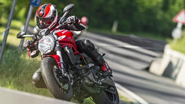 Ein Motorradfahrer fährt auf einer roten Ducati auf einer kurvenreichen Straße.