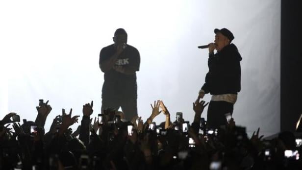 Zwei Rapper treten vor einem Publikum auf, das Handys in die Höhe hält.
