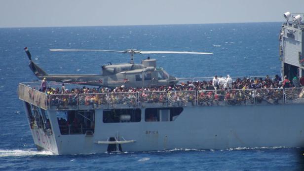 Ein Hubschrauber steht auf einem Schiff, das mit vielen Menschen besetzt ist.