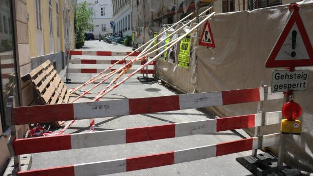 Eine Baustelle blockiert eine Straße mit rot-weißen Absperrungen und Warnschildern.