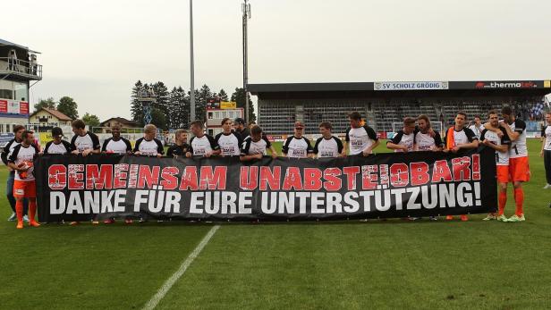 Eine Fußballmannschaft hält ein Banner mit der Aufschrift „Gemeinsam unabsteigbar! Danke für eure Unterstützung!“.