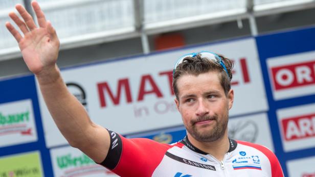 Ein Radrennfahrer winkt mit der Hand in die Menge.