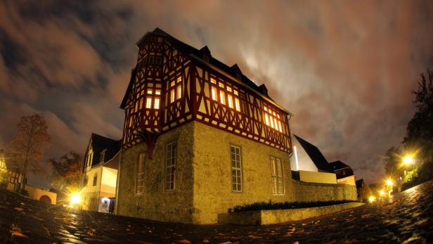 Ein Fachwerkhaus mit beleuchteten Fenstern in einer Stadt bei Nacht.