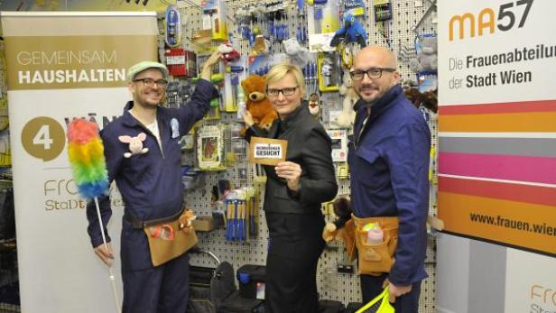 Drei Personen posieren vor einem Regal mit Haushaltswaren und einem Schild der MA57, der Frauenabteilung der Stadt Wien.