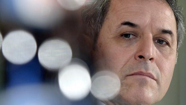 Nahaufnahme eines Mannes mit ernstem Gesichtsausdruck vor unscharfen Lichtern.