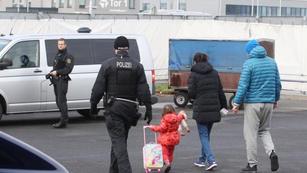 Polizisten begleiten eine Familie mit einem Kind und einem Puppe, die einen kleinen Koffer zieht.