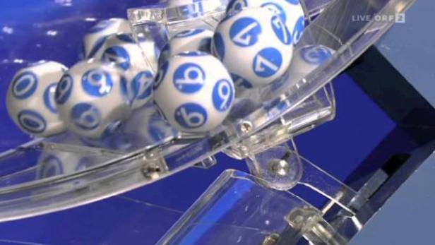 Lotteriebälle mit blauen Zahlen in einer transparenten Trommel.