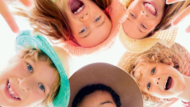 Eine Gruppe lachender Kinder blickt in die Kamera, einige tragen Hüte.