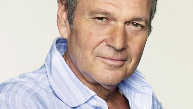 Porträt eines Mannes mit hellblauem Hemd vor einem neutralen Hintergrund.