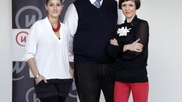 Drei Personen posieren vor einem Banner mit einem stilisierten „W“.