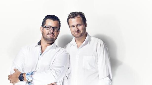Zwei Männer in weißen Hemden posieren vor einem weißen Hintergrund.