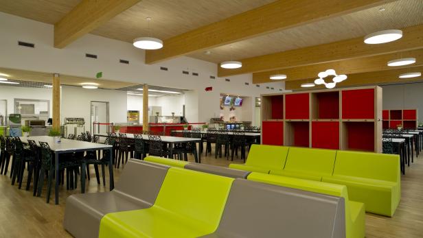 Ein Speisesaal mit Holzbalkendecke, Tischen, Stühlen und farbigen Sitzbänken.