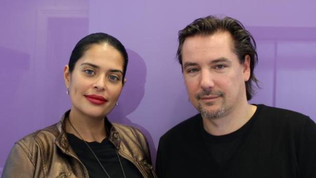 Eine Frau mit rotem Lippenstift und ein Mann posieren vor einer lila Wand.