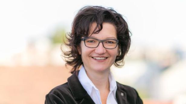 Eine lächelnde Frau mit Brille und dunklem Haar blickt in die Kamera.