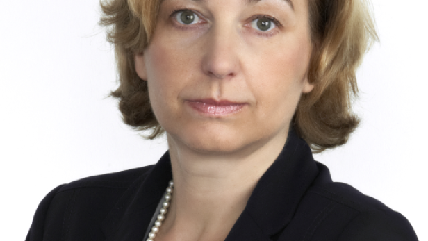 Porträt einer Frau mit blonden Haaren, die eine Perlenkette und einen Blazer trägt.