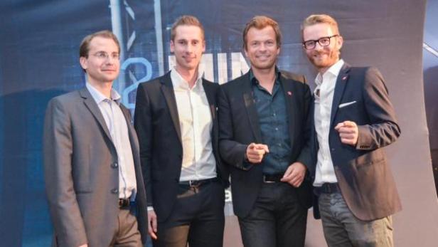 Vier Männer posieren vor einem „PULS 4“-Hintergrund für ein Foto.