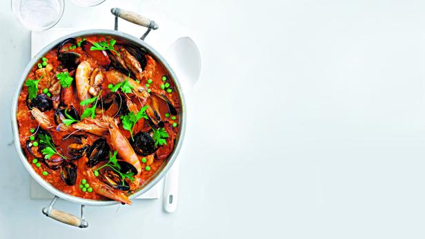 Eine Paella mit Meeresfrüchten, Erbsen und Kräutern in einer großen Pfanne.