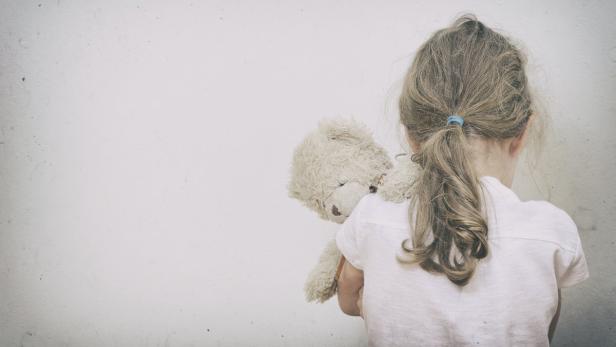 Ein Mädchen umarmt von hinten einen Teddybären.