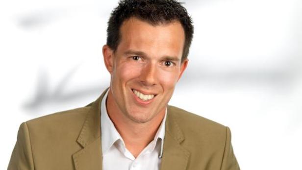 Ein lächelnder Mann in einem hellbraunen Sakko und einem weißen Hemd.