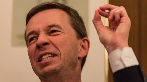 Ein Mann mit Anzug gestikuliert mit zusammengekniffenem Gesichtsausdruck.