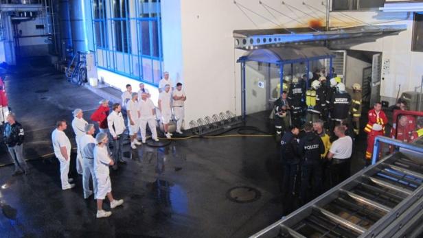 Mitarbeiter in Arbeitskleidung und Rettungskräfte stehen vor einem Gebäude.