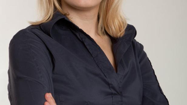 Eine blonde Frau mit verschränkten Armen lächelt in die Kamera.