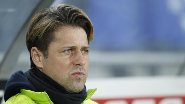 Ein Mann mit blonden Haaren und einer grünen Jacke blickt nachdenklich zur Seite.