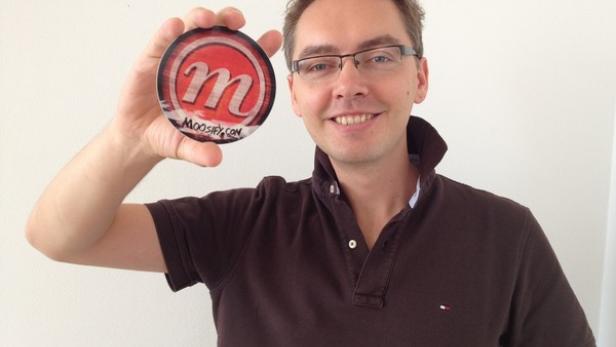 Ein Mann hält einen Aufkleber mit dem Logo von Moosify.com in der Hand.