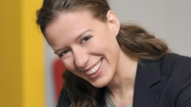 Eine lächelnde Frau mit braunen Haaren und einem dunklen Blazer.