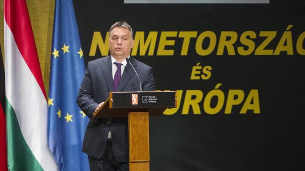 Viktor Orbán hält eine Rede vor Flaggen Ungarns und der EU.