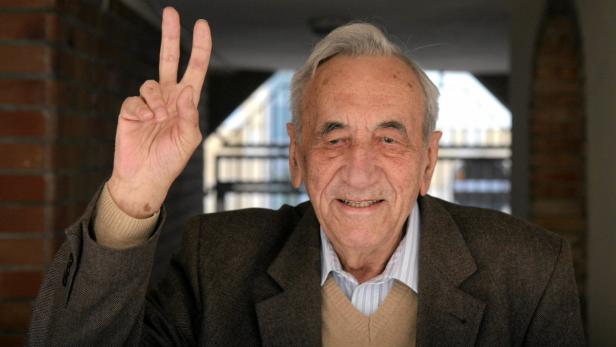 Ein älterer Mann im braunen Jackett zeigt das Victory-Zeichen.