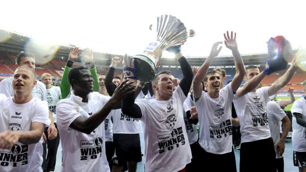 Eine Gruppe Fußballspieler feiert mit der Trophäe in der Hand ihren Sieg.