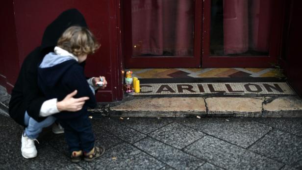 Eine Frau zündet mit einem Kind eine Kerze vor dem „Carillon“ an.
