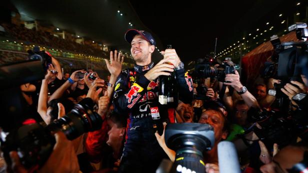 Sebastian Vettel feiert mit einer Champagnerflasche umringt von Fotografen.