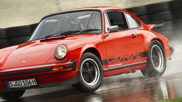 Ein roter Porsche Carrera fährt auf einer nassen Straße.