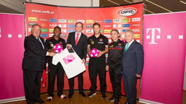 Eine Gruppe von Männern posiert mit einem Trikot und pinkfarbenen Fußbällen vor einem Sponsorenhintergrund.