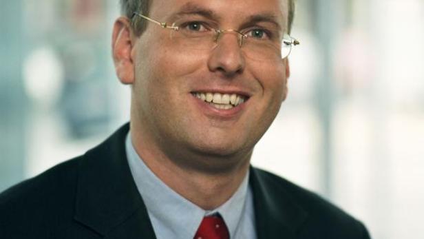 Ein Mann mit Brille, Anzug und roter Krawatte lächelt in die Kamera.