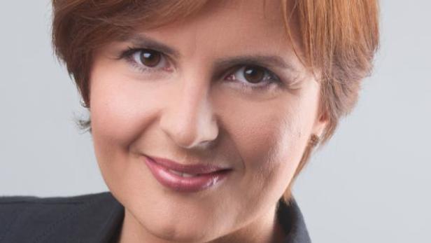 Porträt einer Frau mit braunen Augen und kurzem, rötlichem Haar, die eine dunkle Jacke trägt.