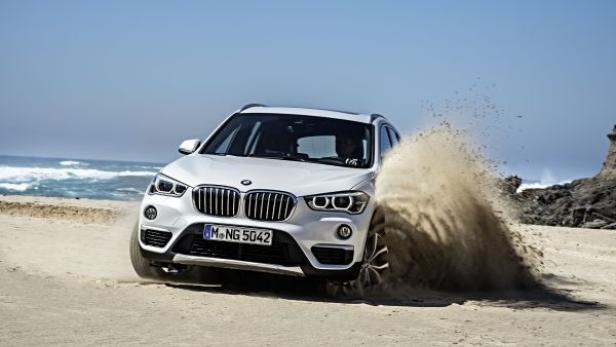 Ein weißer BMW X1 fährt am Strand entlang und wirbelt Sand auf.