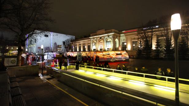 Die Kunsthalle Wien ist nachts hell erleuchtet, während sich Menschen auf einer Eisbahn vergnügen.