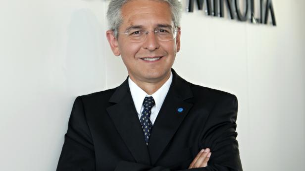 Ein Mann im Anzug steht vor dem Konica Minolta Logo.