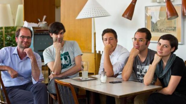 Fünf Personen sitzen an einem Tisch in einem Café und posieren für ein Foto.