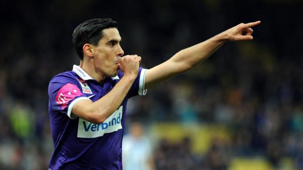 Ein Fußballspieler im lila Trikot jubelt und zeigt mit dem Finger nach rechts.