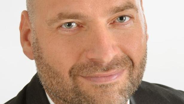 Porträt eines Mannes mit Anzug und Krawatte vor einem neutralen Hintergrund.