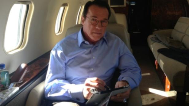 Arnold Schwarzenegger sitzt in einem Privatjet und benutzt ein Tablet.