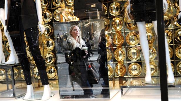 Eine Frau mit einem Getränk spiegelt sich in einem Schaufenster mit goldenen Dekorationen.