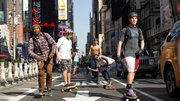 Eine Gruppe von Menschen fährt mit Skateboards und Rollschuhen durch die Strassen von New York.