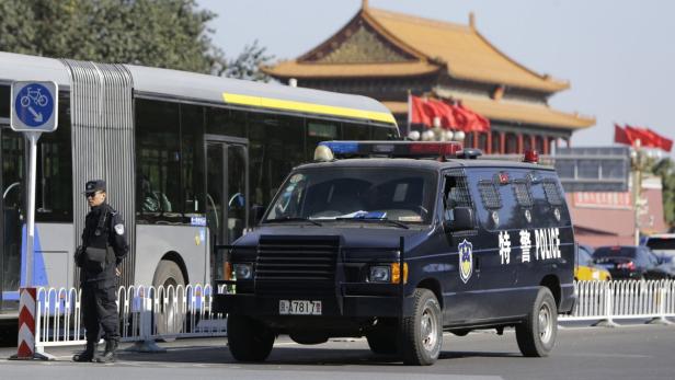 Ein chinesischer Polizist steht neben einem Polizeiwagen vor einem Gebäude mit einem traditionellen Dach.