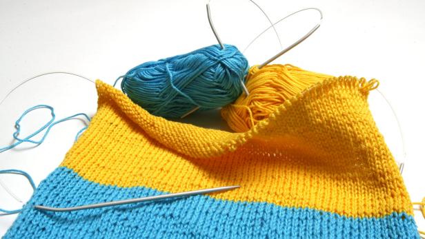 Ein Strickprojekt in Blau und Gelb mit Stricknadeln und Wollknäueln.